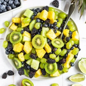 A plate of monochrome fruit salad, with a spoon ready to serve.