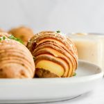 A hasselback potato on a plate, topped with sea salt and chives.