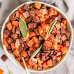 A bowl of oil free herb roasted sweet potatoes garnished with sage.
