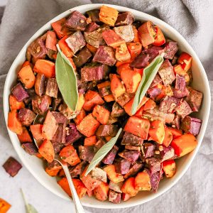 A bowl of oil free herb roasted sweet potatoes garnished with sage.