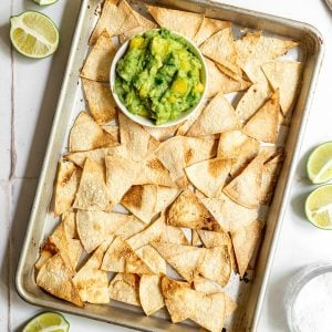 A tray of freshly baked tortilla chips, with a bowl of guac.