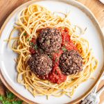 A plate of vegan meatballs served on marinara sauce and pasta.