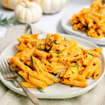 A plate of penne with creamy vegan pumpkin sauce garnished with fresh rosemary.