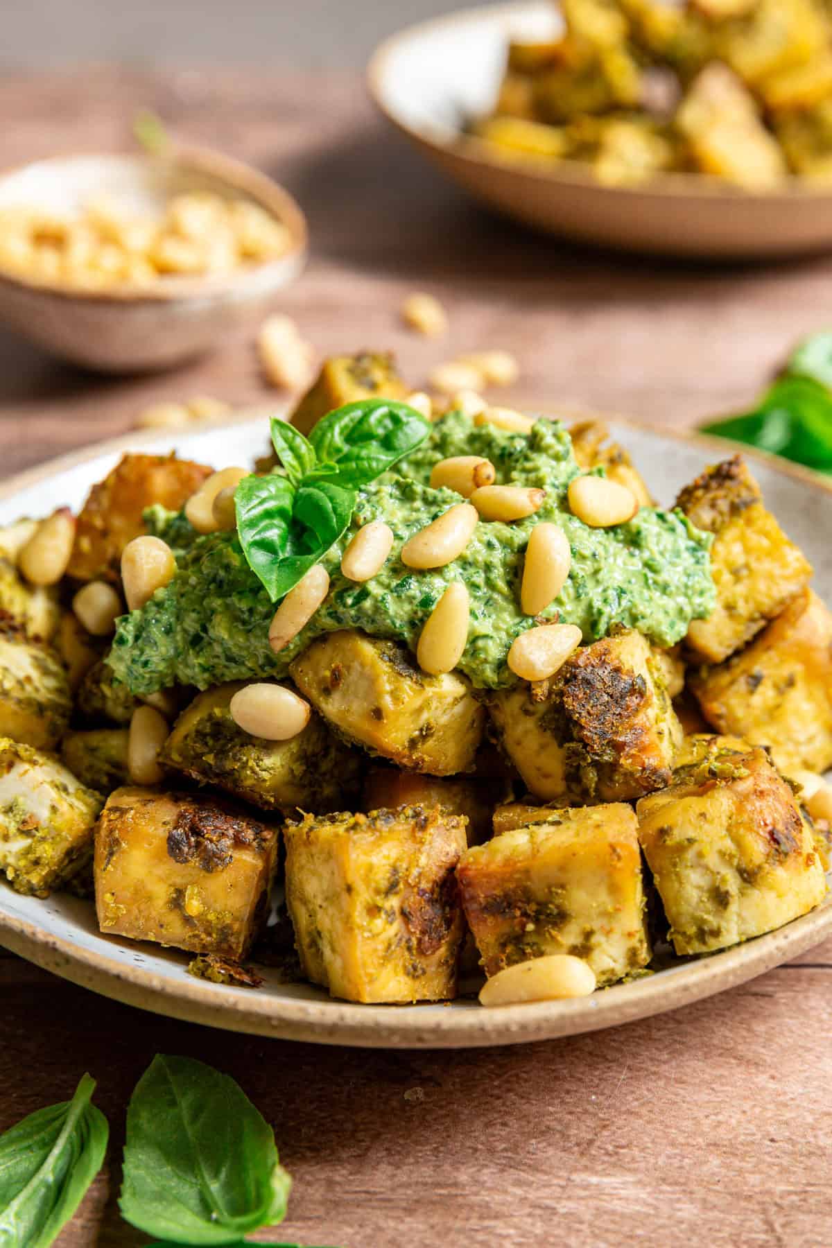 A bowl of pesto tofu with a dollop of pesto, topped with pine nuts and fresh basil.