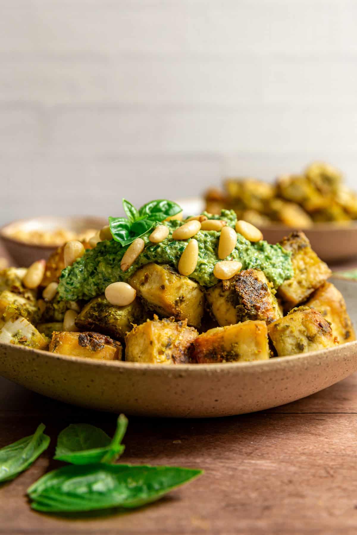 A bowl of pesto tofu with a dollop of pesto, topped with pine nuts and fresh basil.