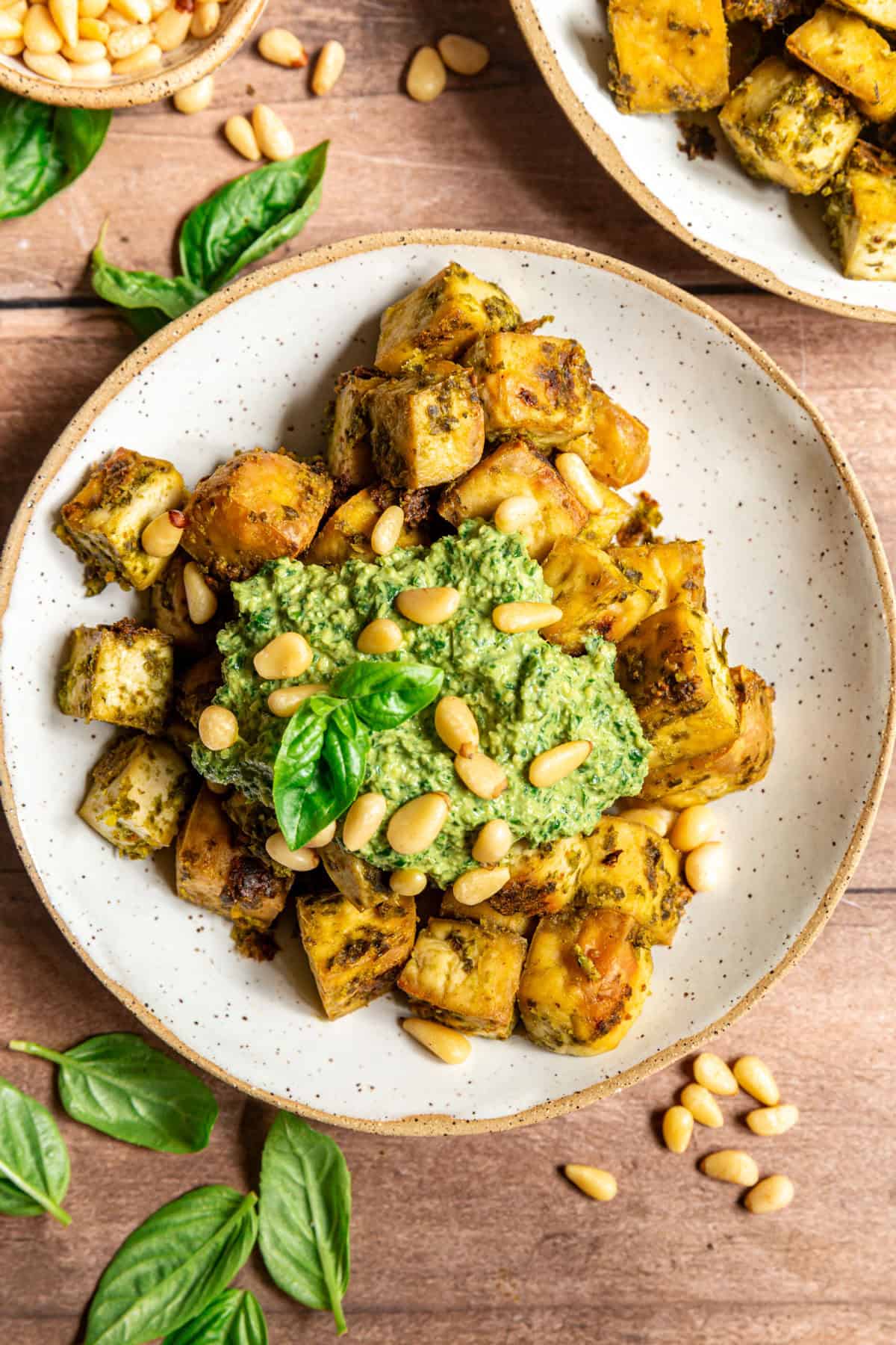 A bowl of pesto tofu with a dollop of pesto, topped with pine nuts and fresh basil.