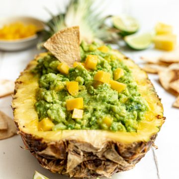 Pineapple mango guacamole served in a pineapple with a tortilla chip dipped inside.
