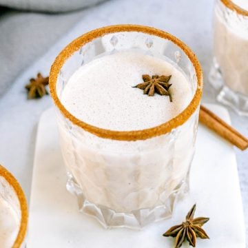 A glass of plant-based eggnog rimmed with cinnamon and topped with star anise.