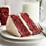 A large slice of red velvet cake, with a fork, ready to serve.
