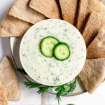 A bowl of plant-based tzatziki on a plate of pita.