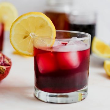 A glass of pomegranate iced green tea, garnished with a lemon slice.