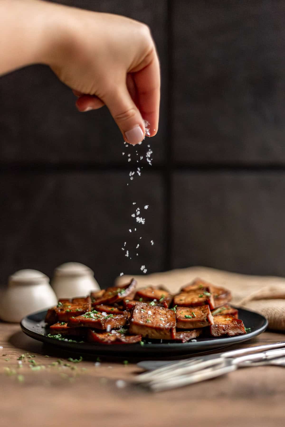 A person sprinkling salt onto smoky tofu.