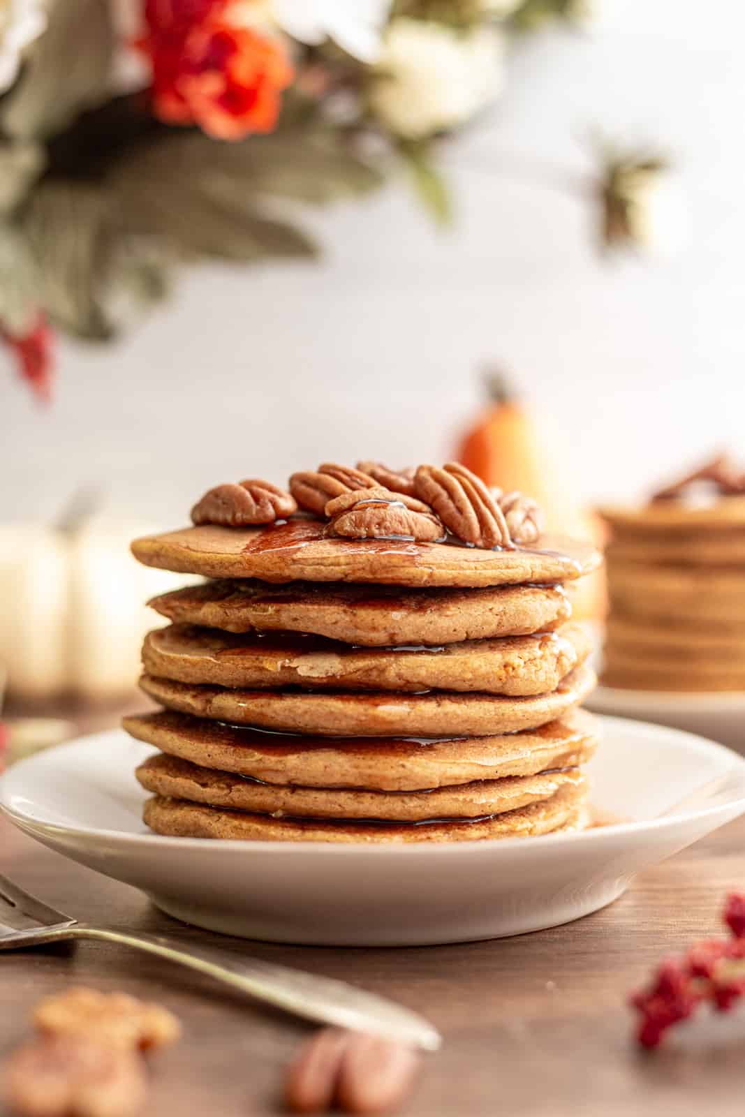 A stack of vegan sweet potato pancakes, topped with pecans and dripping with maple syrup.