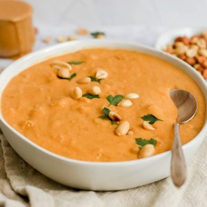 A bowl of sweet potato peanut butter tempeh soup garnished with peanuts and fresh parsley.