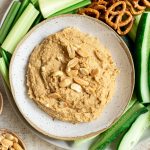 A bowl of Thai peanut hummus on a plate of veggies and pretzels.