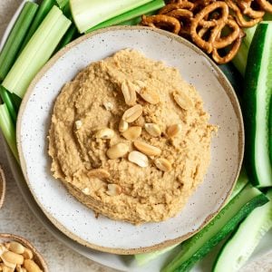 A bowl of Thai peanut hummus on a plate of veggies and pretzels.
