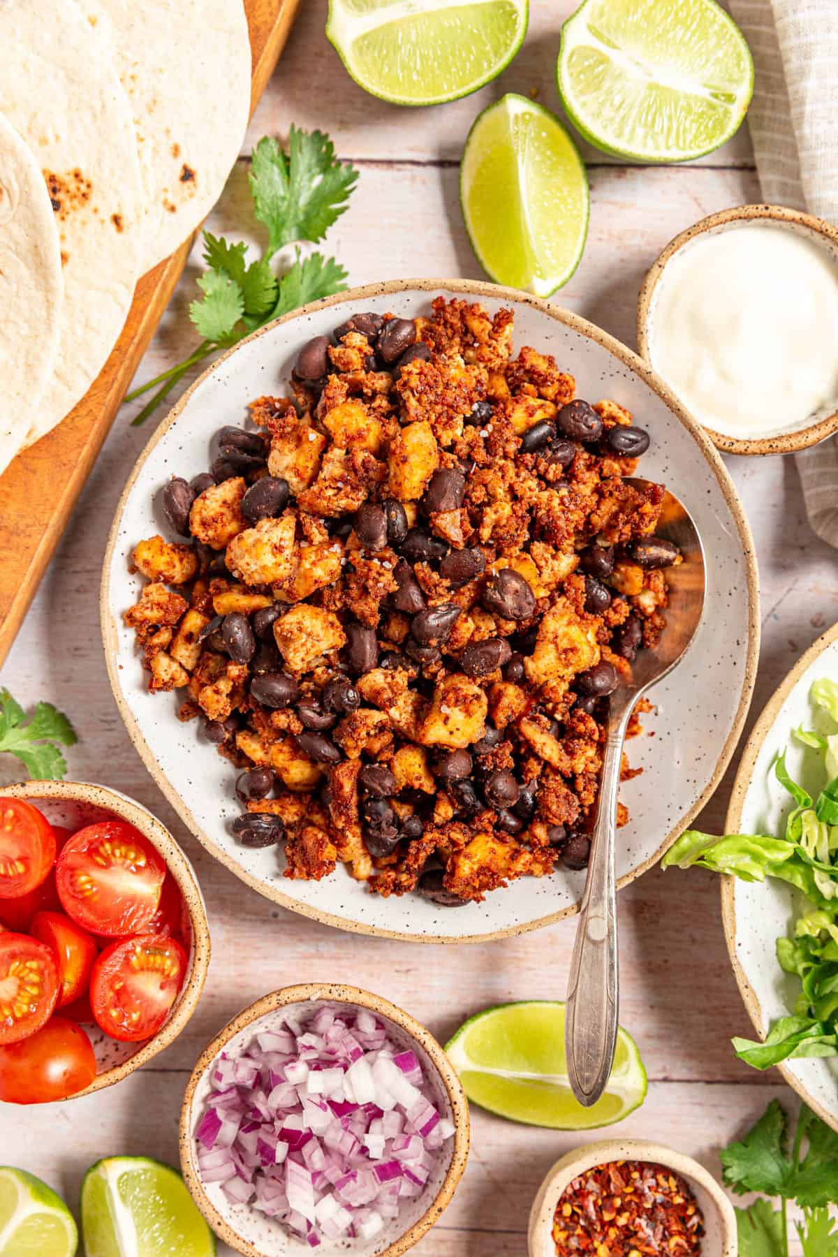 A bowl of tofu crumble tacos surrounded by taco toppings.