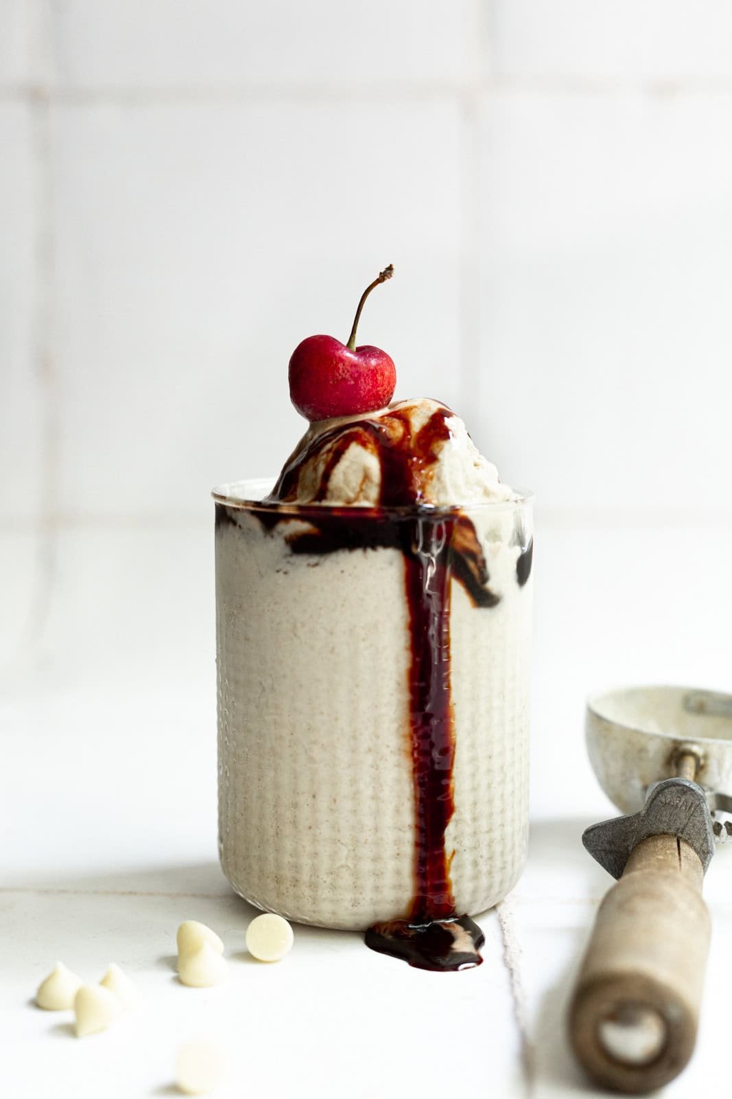 A glass filled with date sweetened no churn vegan vanilla ice cream, drizzled with date syrup and topped with a cherry.