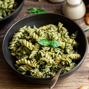 A bowl of vegan almond pesto pasta, garnished with fresh basil.