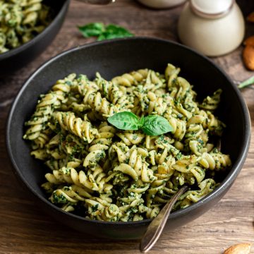 A bowl of vegan almond pesto pasta, garnished with fresh basil.