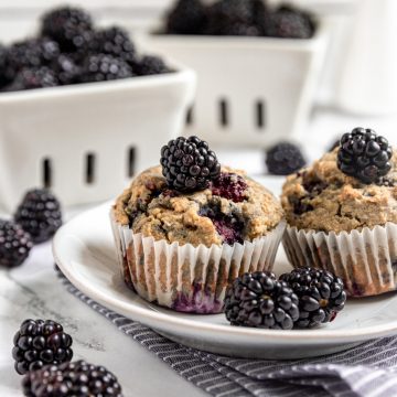 Two vegan blackberry muffins on a plate, served with fresh blackberries.