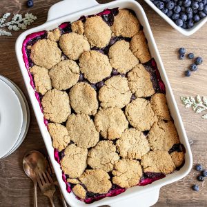 A freshly baked vegan blueberry cobbler, with plates, ready to serve.