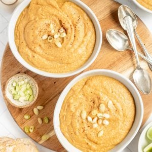 Two bowls of vegan cauliflower leek soup, with scallions, ready to serve.