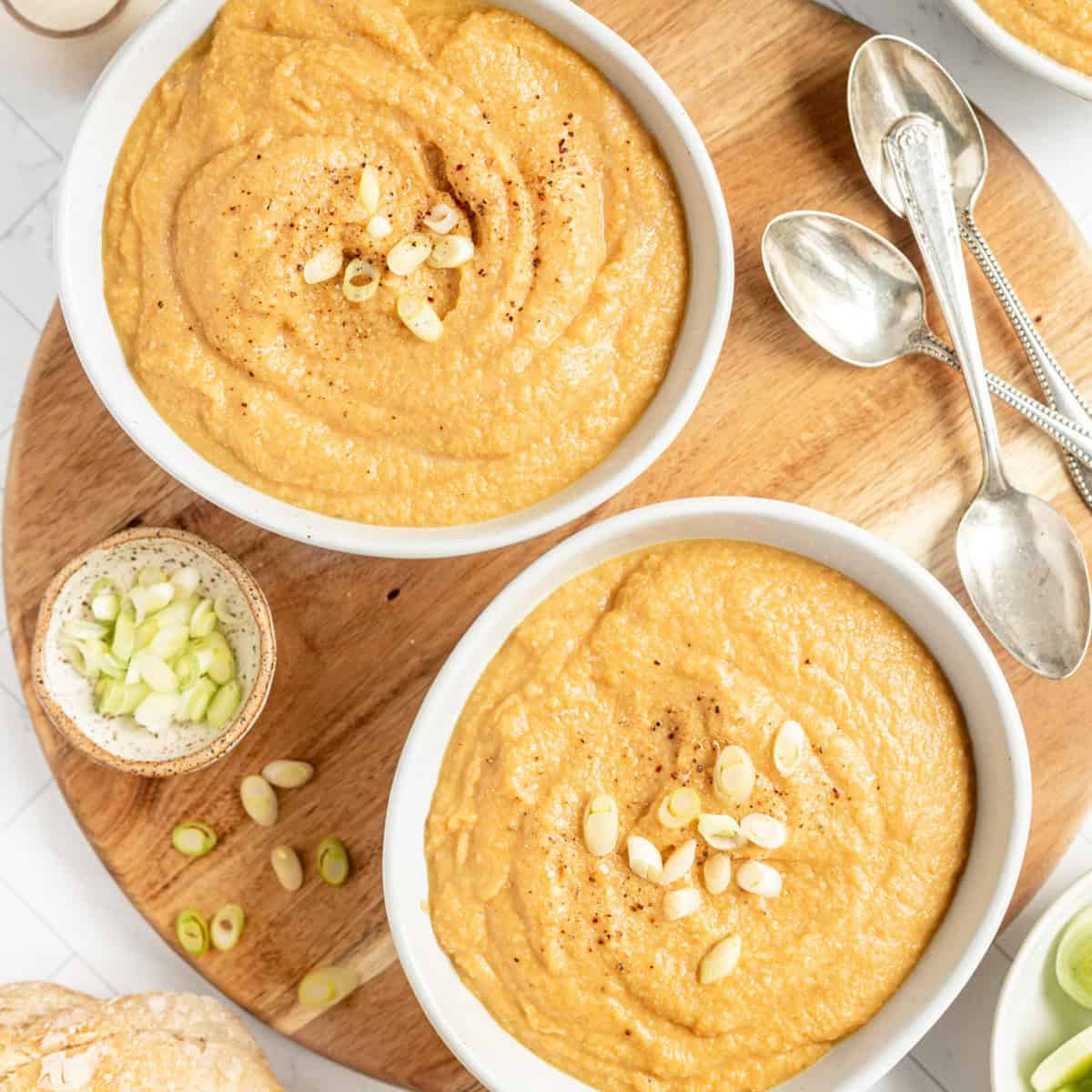 Two bowls of vegan cauliflower leek soup, with scallions, ready to serve.