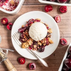 A plate of vegan cherry crumble topped with ice cream.