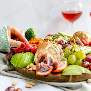 A festively dressed hand picking up a raspberry from the vegan Christmas charcuterie board.