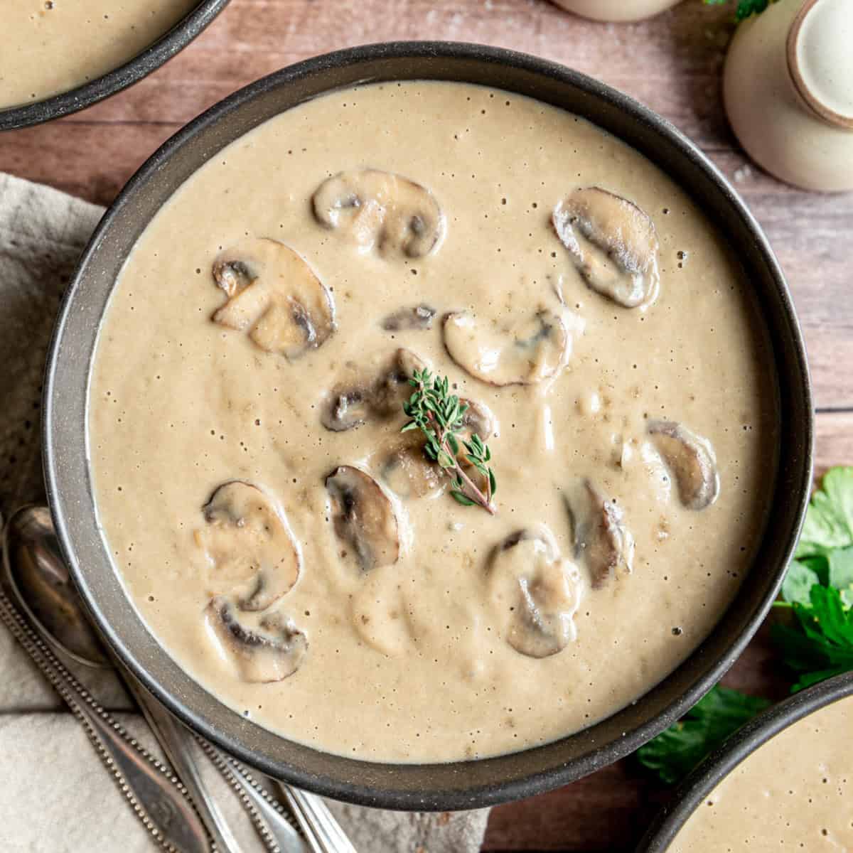 A bowl of vegan cream of mushroom soup, garnished with fresh thyme.