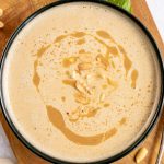 A bowl of vegan cream of peanut butter soup on a cutting board with a spoon, ready to eat.