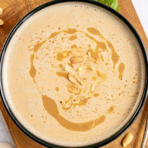 A bowl of vegan cream of peanut butter soup on a cutting board with a spoon, ready to eat.