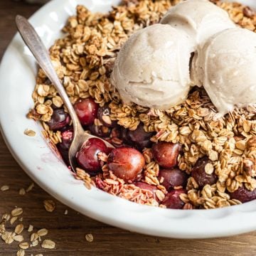 Vegan gluten free cherry crisp with a serving removed, highlighting bright red cherries.