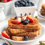 A stack of vegan high protein french toast on a plate, topped with fresh fruit.