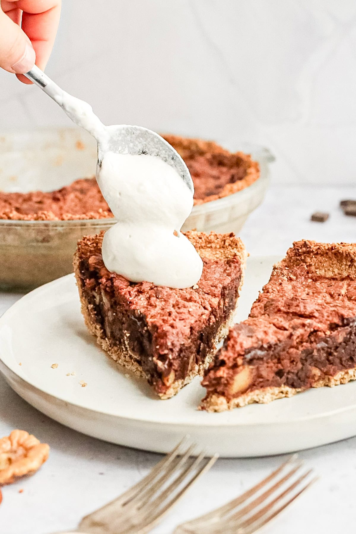 Two slices of plant-based kentucky derby pie being topped with whipped cream.