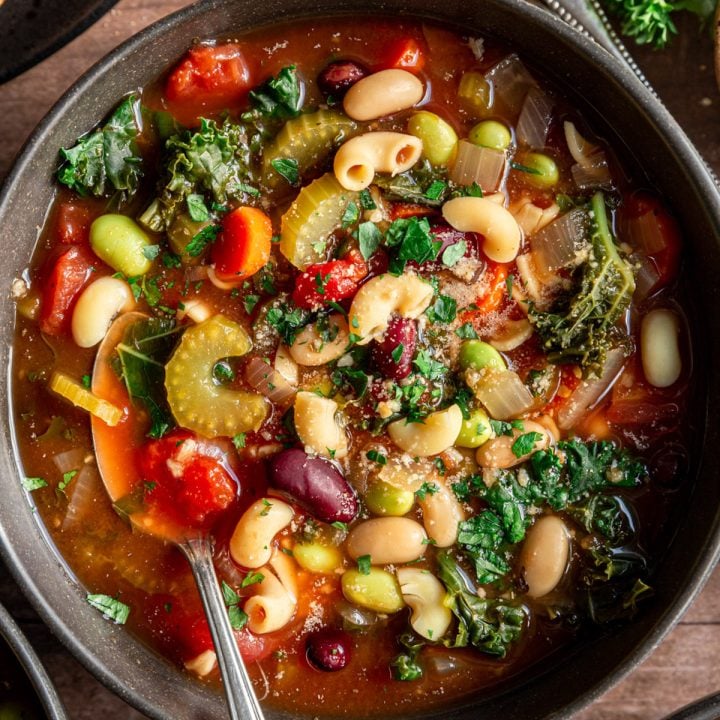 A bowl of vegan minestrone soup, with a spoon, ready to serve.