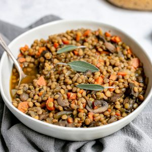 A bowl of mushroom lentil stew with a spoon, ready to eat.