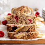 A loaf of vegan oat flour raspberry banana bread with two slices cut.
