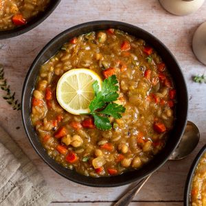 A bowl of vegan orzo soup, garnished with a lemon slice.