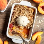 Peach crisp with a serving removed and a scoop of ice cream on top
