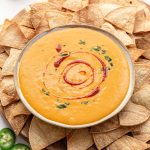 A bowl of vegan queso on a tray of chips.
