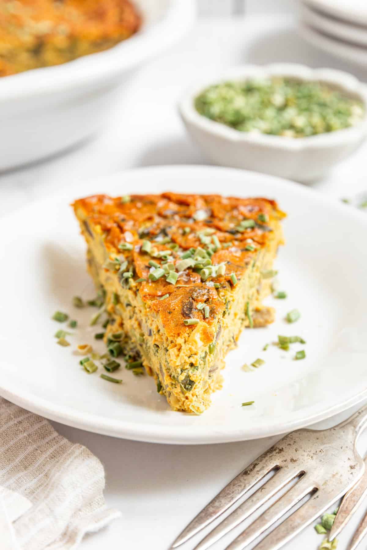 A slice of vegan crustless quiche topped with fresh chives.