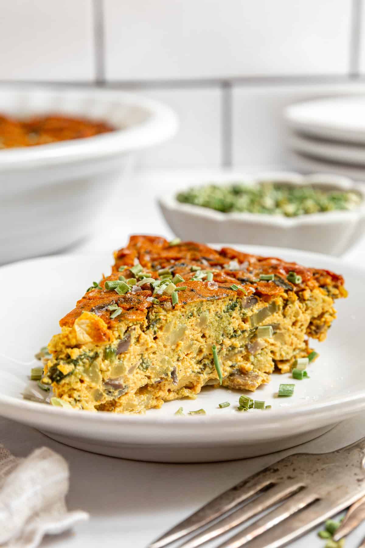 A slice of vegan crustless quiche topped with fresh chives.