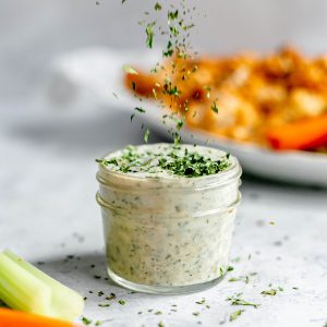 Herbs sprinkled into a jar of vegan ranch.