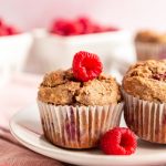 A raspberry muffin on a plate with fresh raspberries.