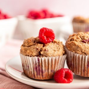 A raspberry muffin on a plate with fresh raspberries.