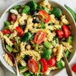 A bowl of vegan pasta salad with serving utensils.