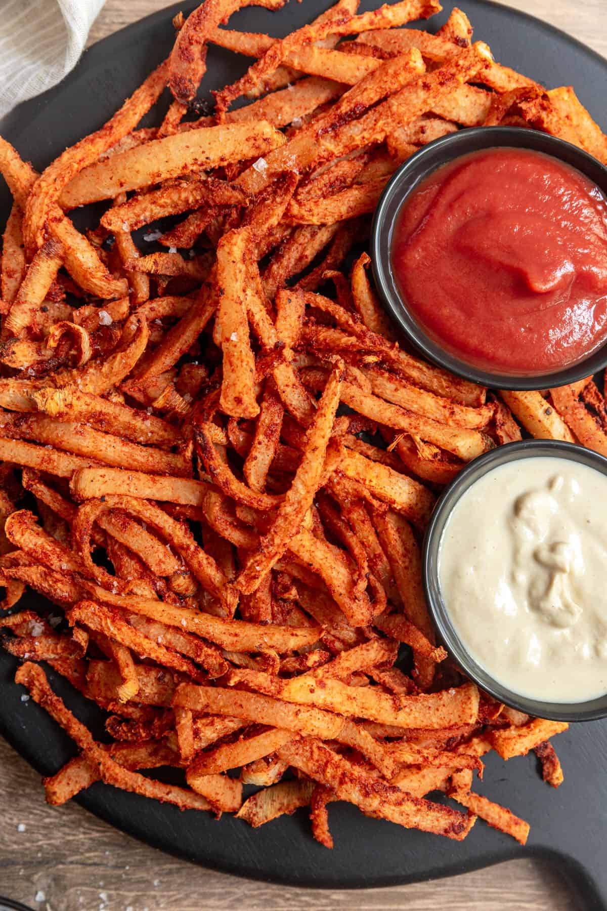 Jicama air fryer fries on a serving board with bowls of ketchup and mayo.