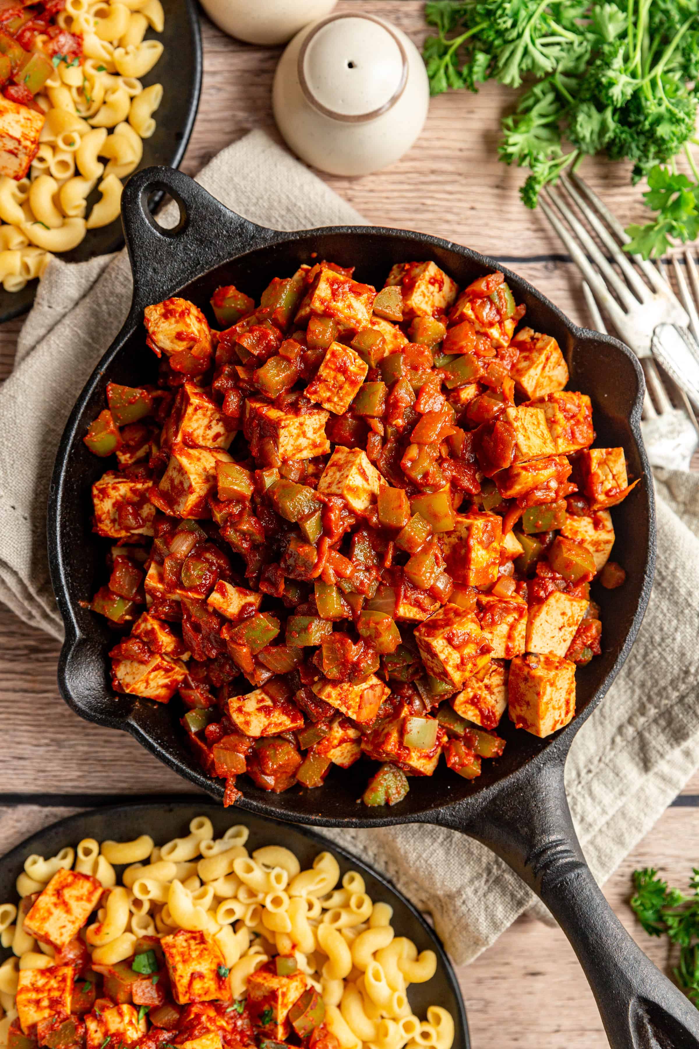 Vegan Paprikash in a skillet with plated dishes surrounding it.